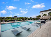 Thumbnail 13 of 45 - A large outdoor swimming pool with sun loungers and a building in the background.