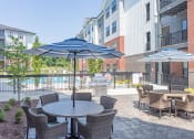 Thumbnail 17 of 18 - Apartments For Rent In Hermitage, TN - Outdoor Patio Area By The Pool. Patio Has Gas BBQ Grills, Tables With Umbrellas, Chairs, And Maintained Landscaping.