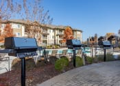 Thumbnail 24 of 30 - an outdoor pool with barbecue grills and chairs in front of an apartment building
