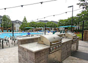 Thumbnail 35 of 59 - A pool with a barbecue grill and chairs is surrounded by apartment buildings.
