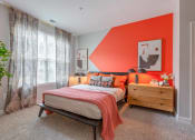 Thumbnail 6 of 20 - a bedroom with an orange accent wall and a bed with a wooden dresser and bedside