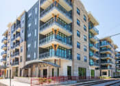 Thumbnail 1 of 47 - Pet Friendly Apartments in Downtown Memphis TN - The Landing Residences - Corner Street View of Buidling Beside Trolley Tracks with Stone and Grey Details, and Showcasing Balconies