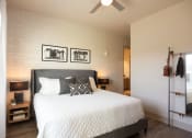 Thumbnail 6 of 47 - 1 BR Apartments in Downtown Memphis TN - The Landing Residences - Furnsihed Bedroom wtih Hardwood Floor, Bed, Nightstands with Lamps, Standing Mirror with Storage, Ceiling Fan, White Painted Brick Accent Wall, and Attached Bathroom