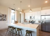 Thumbnail 3 of 47 - Luxury Apartments in Downtown Memphis TN - The Landing Residences - Spacious and Modern Kitchen with White Quartz Countertops, Stainless Steel Appliances, Geometric Tile Backsplash, Large Cooking Island with Seating and Hanging Overhead Lights, Hardwood Floor, and Light Cabinetry