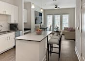 Thumbnail 8 of 22 - A kitchen with white cabinets and a large island with a bowl of fruit on it.