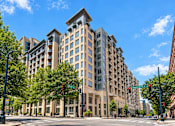 Thumbnail 1 of 33 - A large, modern building with many windows is situated on a street corner.