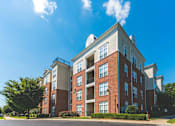 Thumbnail 22 of 25 - A large red brick apartment building with a white roof and a balcony on the second floor.