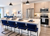 Thumbnail 13 of 30 - A kitchen with a long white island and blue chairs.