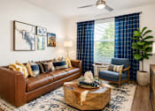 Thumbnail 15 of 30 - A living room with a brown leather couch, a coffee table with a gift box on it, a blue chair, and a ceiling fan.