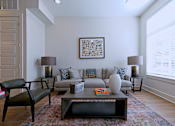 Thumbnail 7 of 32 - One Bedroom Apartments in Memphis, TN - The Rise - Living Room with Plush Gray Couch, Two Round Side Tables with Lamps, Wooden Coffee Table, Wide Leather-Style Chair, Hardwood-Style Flooring, Area Rug, and Large Window with White Blinds.