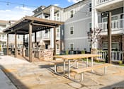 Thumbnail 35 of 50 - Three-Bedroom Luxury Apartments in Alcoa, TN - Vintage Hunters Crossing - Outdoor Patio with Grilling Stations, Pergola, Picnic Table, String Lights, Metal Fence, and View of the Apartments.