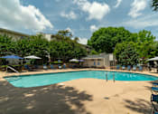 Thumbnail 20 of 35 - A large swimming pool surrounded by trees and a building in the background.