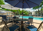 Thumbnail 22 of 35 - A table with chairs and an umbrella is in the foreground of a pool area.