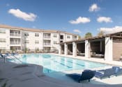 Thumbnail 32 of 35 - a swimming pool with blue chairs and an apartment building in the background