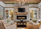 Thumbnail 3 of 44 - A living room with a stone fireplace and a chandelier.