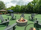 Thumbnail 27 of 35 - A fire pit sits in the middle of a green lawn surrounded by chairs.