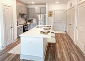 Thumbnail 30 of 70 - A kitchen with a white island and wooden floors.