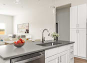 Thumbnail 64 of 79 - A modern kitchen with a stainless steel sink and a bowl of fruit on the counter.