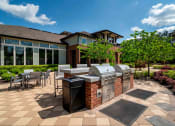 Thumbnail 24 of 36 - One BR Apartments in Greenville SC - Velo Verdae - Outdoor Grill Station with Brick and Stainless Steel Grill Sets, Counter with Bar Chairs, Table Seating, and Surrounding Trees
