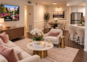 Thumbnail 9 of 20 - A living room with a television, a dining table, and a kitchen area.