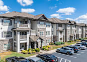 Thumbnail 27 of 31 - an apartment building with cars parked in a parking lot