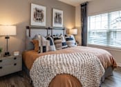 Thumbnail 12 of 60 - 3-Bedroom Apartments in Brunswick, GA - Vintage Brunswick - Bedroom with Hardwood-Inspired Flooring, Large Bed, Nightstands with Lamps, and Large Window