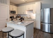 Thumbnail 4 of 60 - Two-Bedroom Apartments in Brunswick, GA - Vintage Brunswick - Kitchen with Hardwood-Inspired Flooring, Quartz Countertops, Tile Backsplash, Stainless Steel Appliances, White Cabinetry, and Kitchen Island with Stool Seating