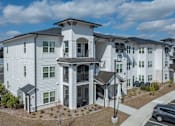 Thumbnail 59 of 60 - Pet-Friendly Apartments in Brunswick, GA - Vintage Brunswick - Property Exterior with White Walls, Manicured Plant Beds, and View of Parking Area