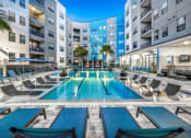 Thumbnail 21 of 48 - an apartment swimming pool with lounge chairs in front of an apartment building