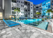Thumbnail 34 of 48 - an apartment pool with blue lounge chairs in front of an apartment building
