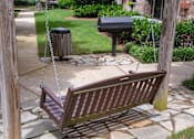 Thumbnail 18 of 23 - A wooden swing bench is suspended from chains in a backyard.