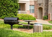 Thumbnail 19 of 23 - A black mailbox sits on a post next to a picnic table in front of a brick building.