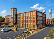 Thumbnail 1 of 27 - A large red brick building with a water tower in the background.