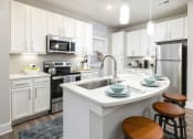 Thumbnail 3 of 29 - Apartments Near Santa Rosa Beach in Panama City Beach, FL - The Tyde - Kitchen with Hardwood-Style Flooring, Kitchen Island with Seating, Quartz Countertops, Designer Ceramic Tile Backsplash, GE Stainless Steel Appliances, and White 42-Inch Cabinets.