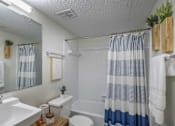 Thumbnail 15 of 36 - A bathroom with a white sink, toilet, and a blue and white striped shower curtain.