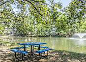 Thumbnail 27 of 36 - A blue picnic table is set up by a pond with a fountain in the background.