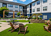 Thumbnail 25 of 29 - A sunny day at a residential complex with a hammock, picnic table, and chairs.