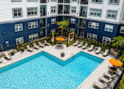Thumbnail 1 of 29 - A large swimming pool surrounded by lounge chairs and umbrellas in front of a multi-story building.