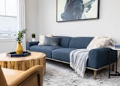 Thumbnail 9 of 29 - A living room with a blue couch and a yellow vase on a wooden table.