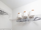 Thumbnail 13 of 29 - A white closet with grey carpet and two shelves with hangers and jars.