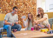 Thumbnail 10 of 34 - Three people playing a card game on a wooden table.