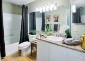 Thumbnail 29 of 32 - Luxury Apartments For Rent In Columbus - Bathroom With Wood-Style Flooring, Large Vanity With Lighting, Granite Countertops, White Cabinets, Sink, Toilet, And Shower With A Tub.