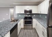 Thumbnail 22 of 32 - Columbus, GA Luxury Apartments - Kitchen With Wood-Style Flooring, Granite Countertops, Stainless Steel Appliances, Goose-Neck Sink, Dishwasher, Built-In Microwave, And White Cabinets.