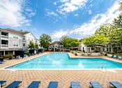 Thumbnail 22 of 30 - A large swimming pool surrounded by blue lounge chairs and apartment buildings.