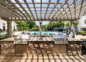 Thumbnail 25 of 30 - A grill is built into a stone wall under a wooden pergola.