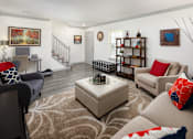 Thumbnail 8 of 30 - A living room with a rug, a couch, a chair, a coffee table, and a staircase.