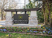 Thumbnail 26 of 31 - A sign for Wildwood Apartments is surrounded by flowers and greenery.
