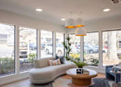 Thumbnail 17 of 31 - A living room with a grey couch, a wooden coffee table, and a large window with a view of a parking lot.