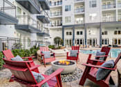 Thumbnail 21 of 22 - A poolside area with red chairs and a fire pit.
