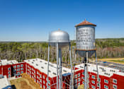 Thumbnail 29 of 33 - Two large water towers are situated in front of a red brick building.
